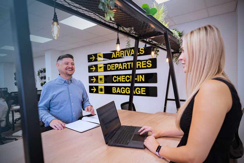 Two agents talking across a desk under airport-style signage
